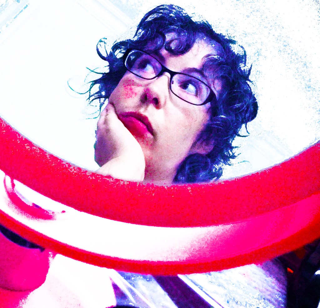 A white woman with black curly hair and glasses looks thoughtful